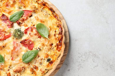 Tasty quiche with cheese, tomatoes and basil leaves on light grey table, top view. Space for text