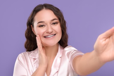 Photo of Smiling woman with braces taking selfie on violet background