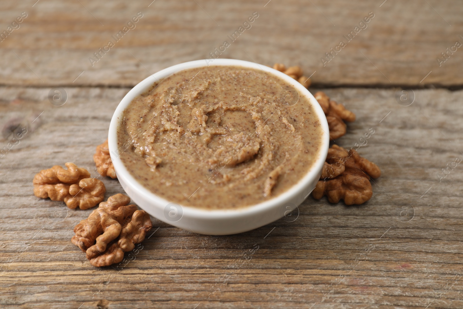 Photo of Delicious nut butter in bowl and walnuts on wooden table, closeup