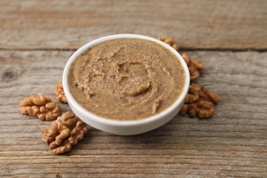 Delicious nut butter in bowl and walnuts on wooden table, closeup