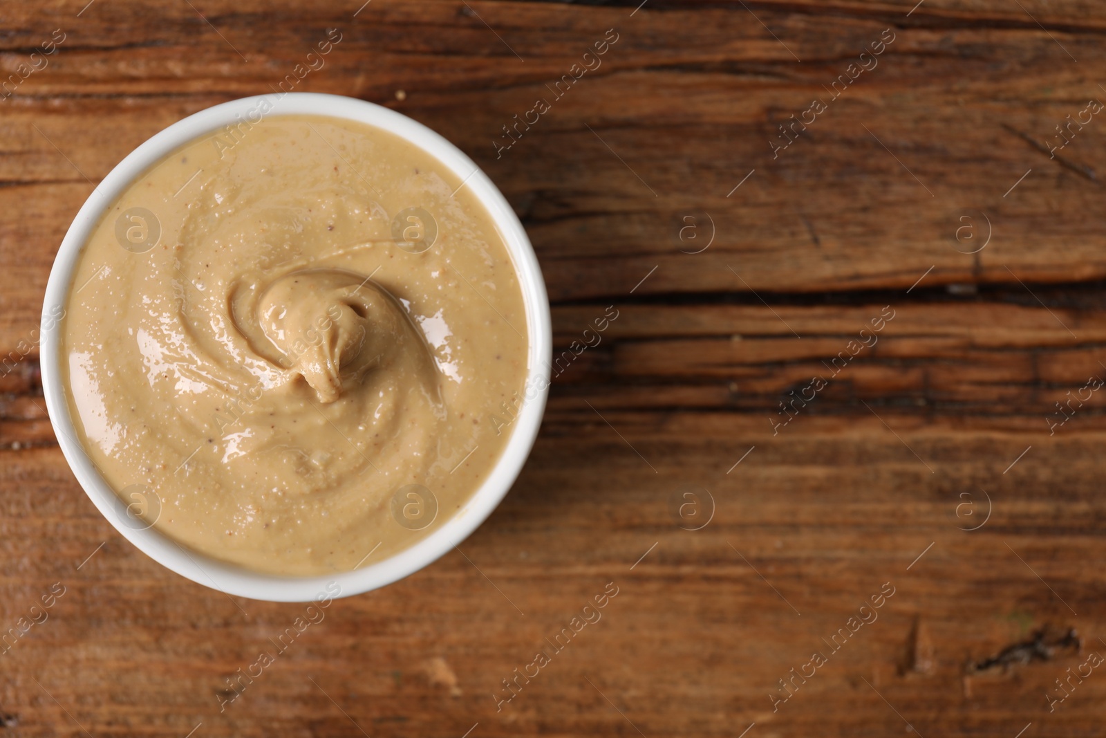 Photo of Delicious nut butter in bowl on wooden table, top view. Space for text