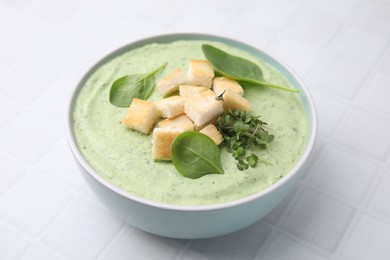 Delicious spinach cream soup with croutons in bowl on white tiled table