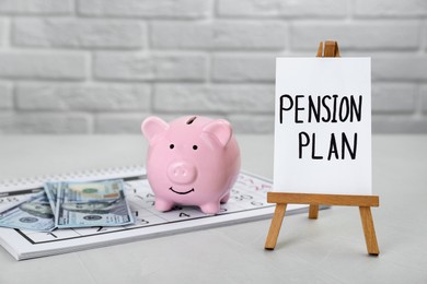 Photo of Card with phrase Pension Plan, piggy bank and dollar banknotes on white table