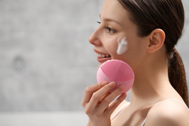 Young woman washing face with brush and cleansing foam indoors. Space for text