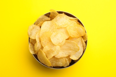 Delicious crispy potato chips in bowl on color background, top view