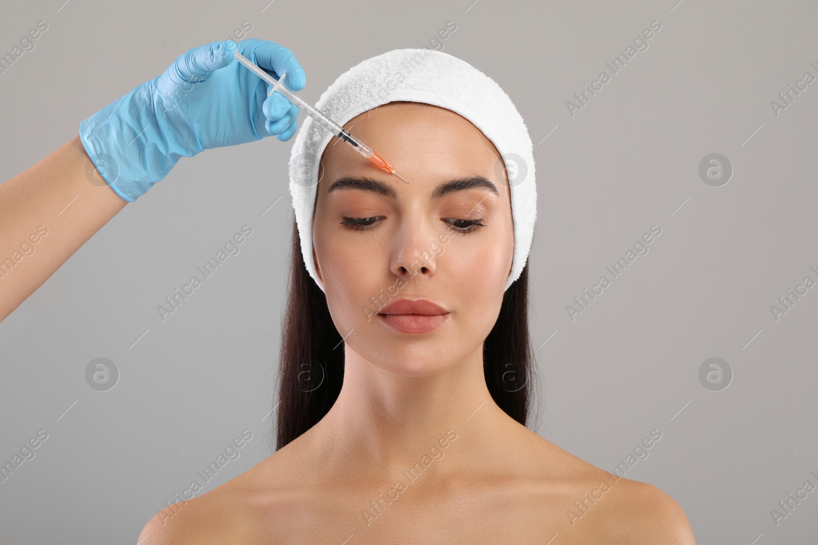 Photo of Doctor giving facial injection to young woman on light grey background. Cosmetic surgery