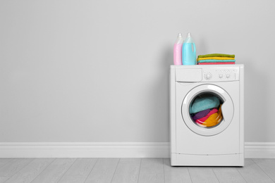 Modern washing machine with stack of towels and detergents near white wall, space for text. Laundry day