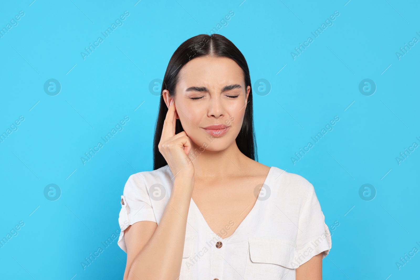 Photo of Young woman suffering from ear pain on light blue background