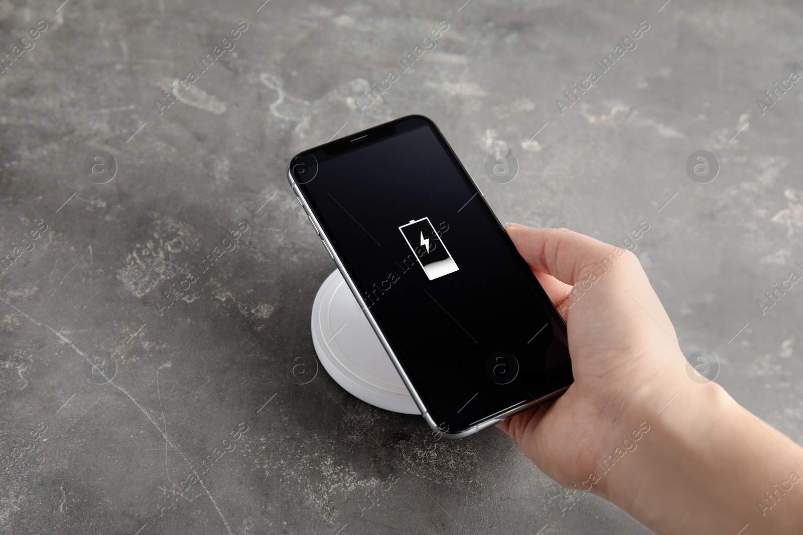 Photo of Woman putting mobile phone onto wireless charger at  grey table, closeup