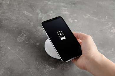Photo of Woman putting mobile phone onto wireless charger at  grey table, closeup