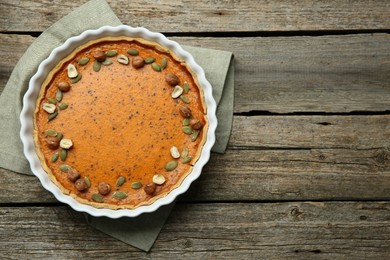 Delicious pumpkin pie with seeds and hazelnuts on wooden table, top view. Space for text