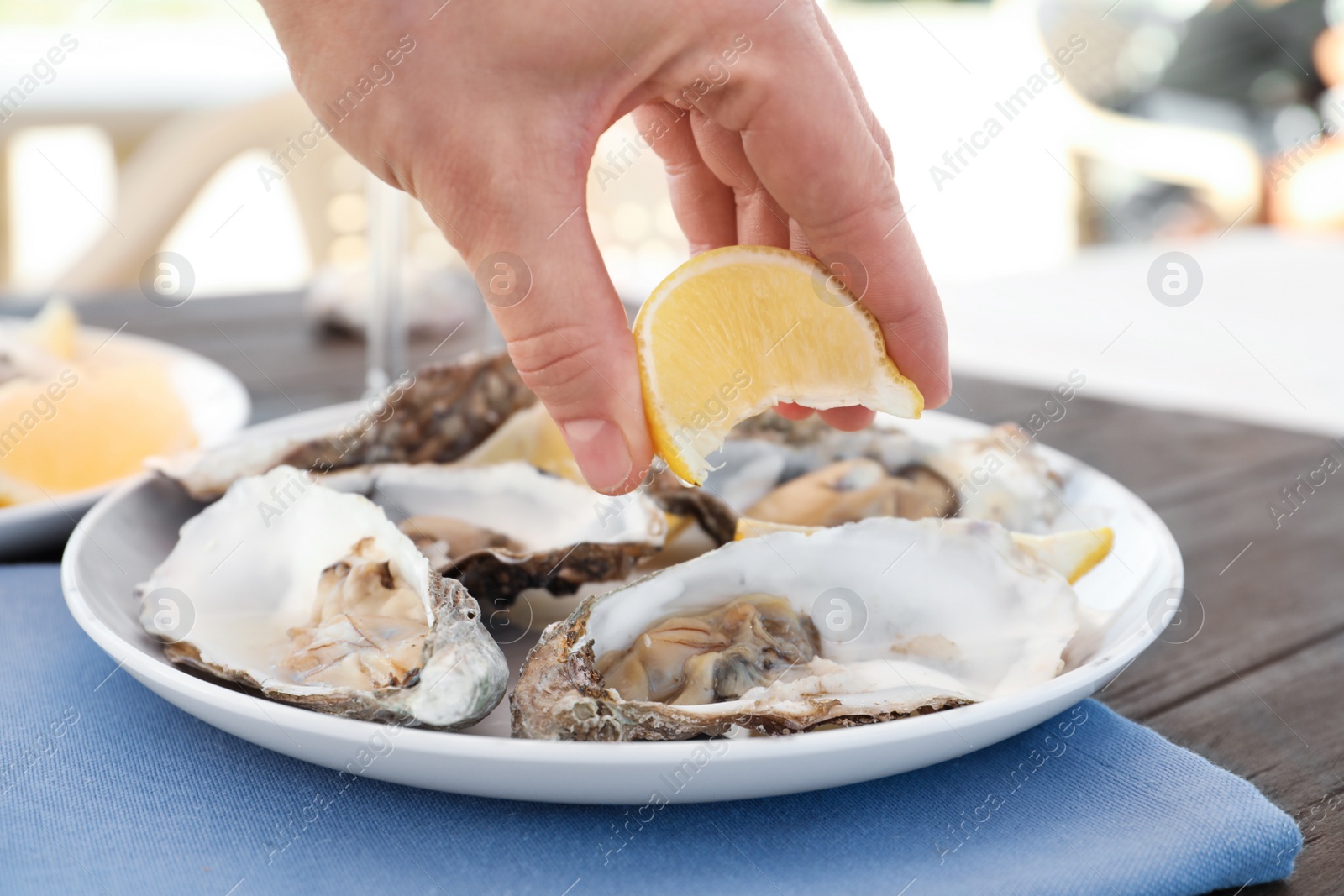 Photo of Woman squeezing lemon onto fresh tasty oysters on plate