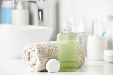 Photo of Mouthwash, towel and dental floss on white countertop in bathroom
