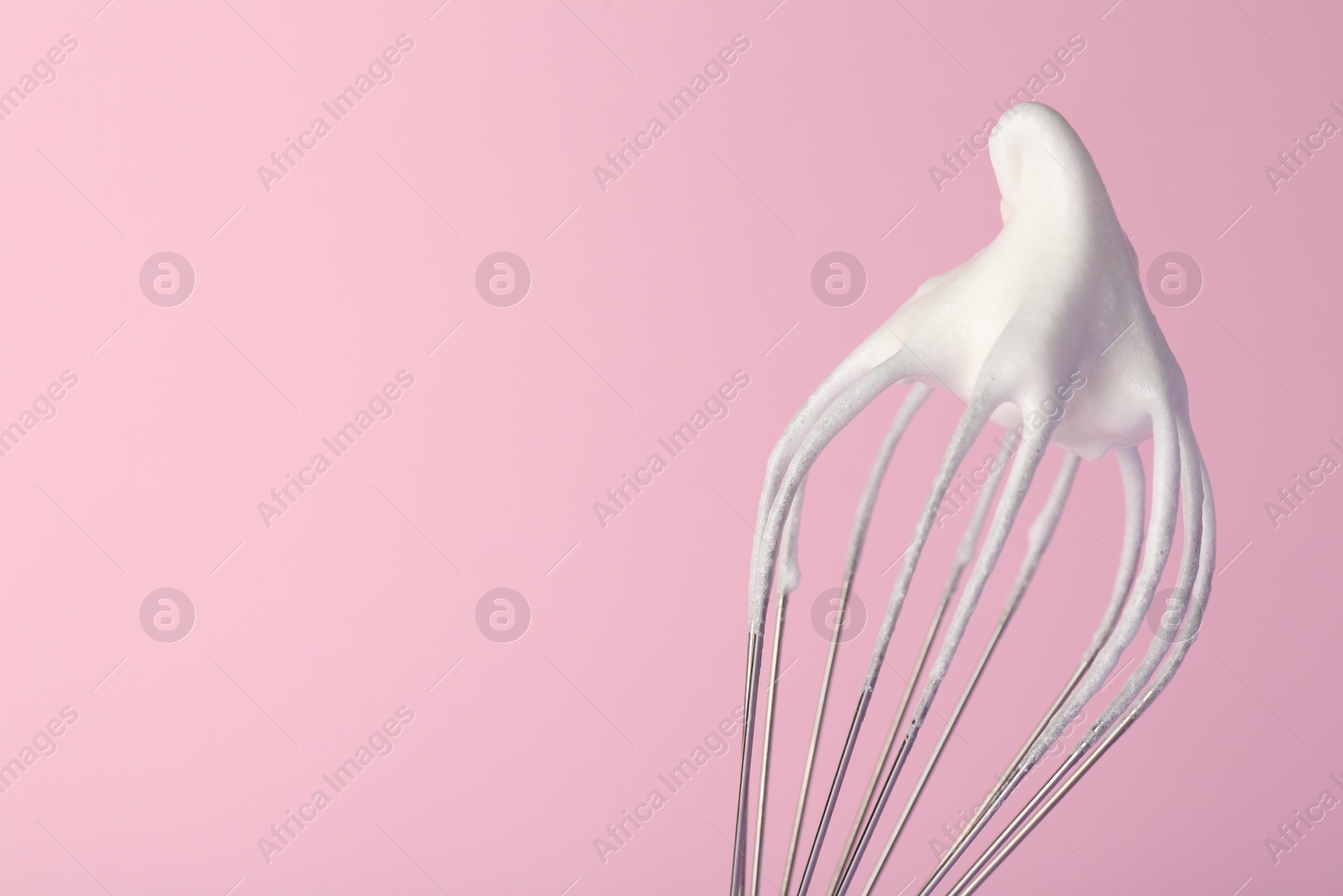 Photo of Whisk with whipped egg whites on pink background, closeup. Space for text