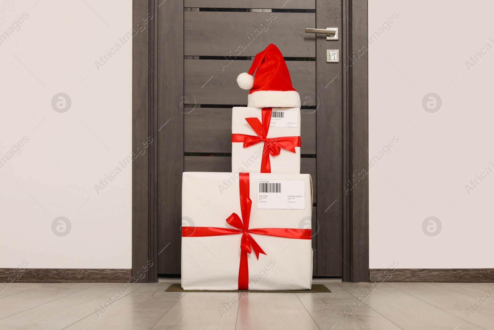 Photo of Christmas gift boxes and Santa hat near door indoors. Sending present by mail