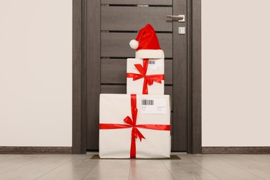 Photo of Christmas gift boxes and Santa hat near door indoors. Sending present by mail