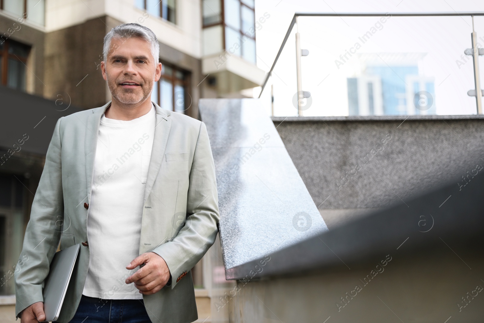 Photo of Portrait of handsome mature man with laptop in city center. Space for text