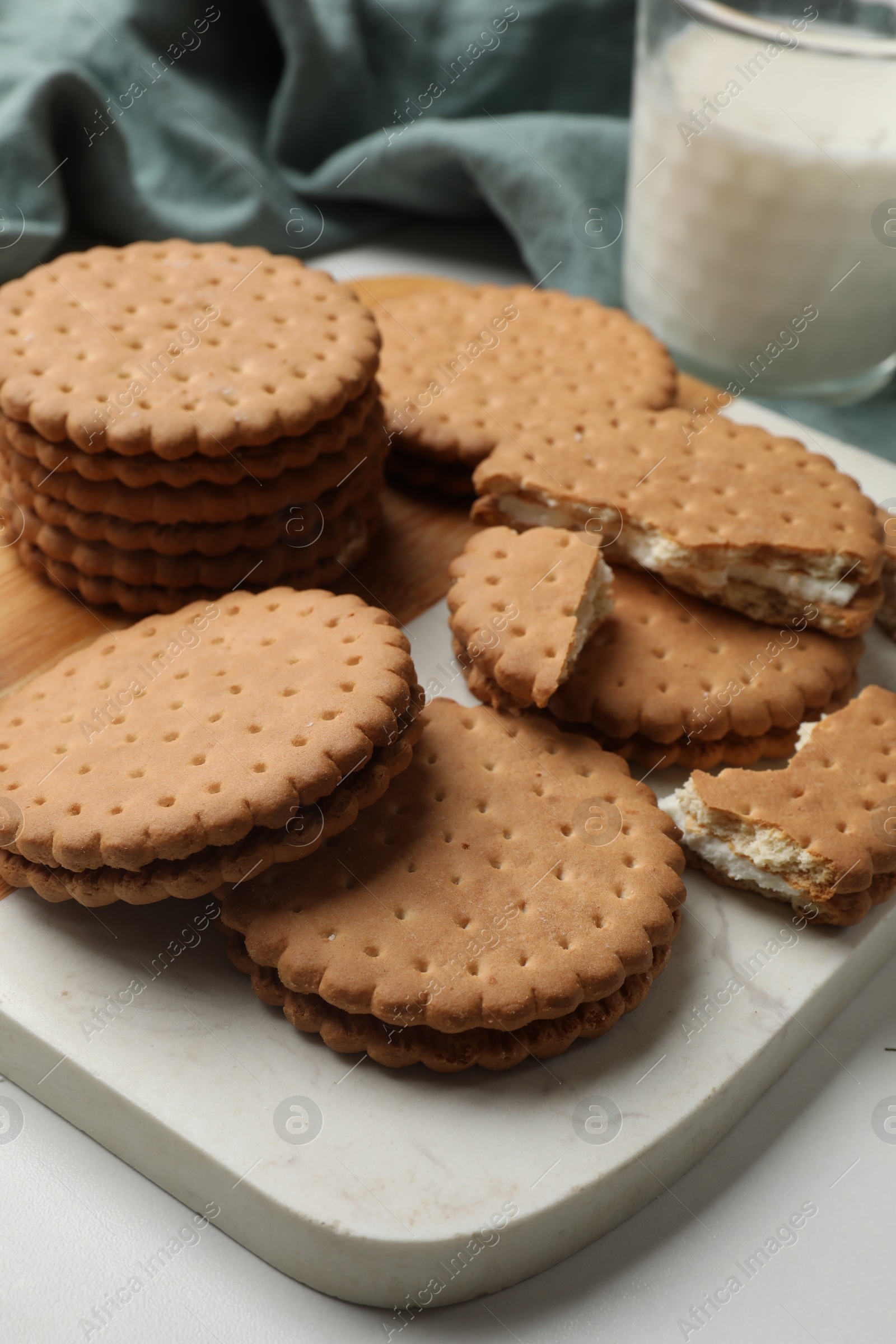 Photo of Tasty sandwich cookies and glass of milk on white table, closeup