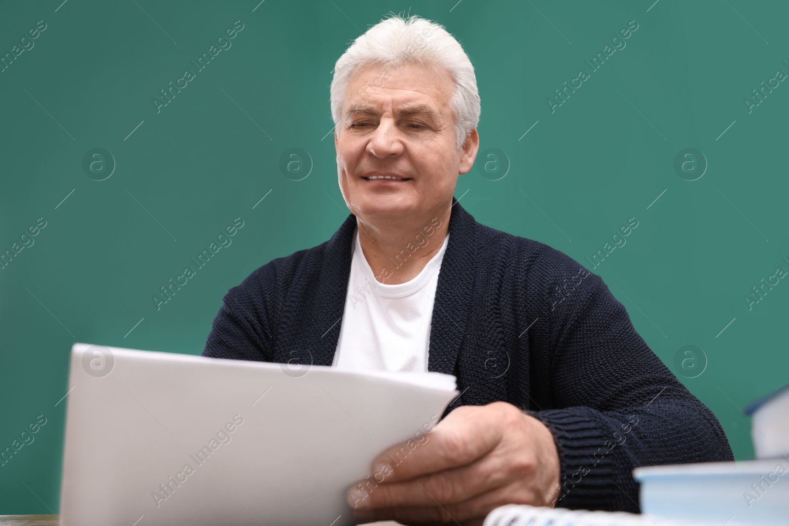 Photo of Portrait of senior teacher at table against green chalkboard