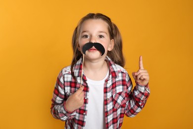 Funny little girl with fake mustache on yellow background