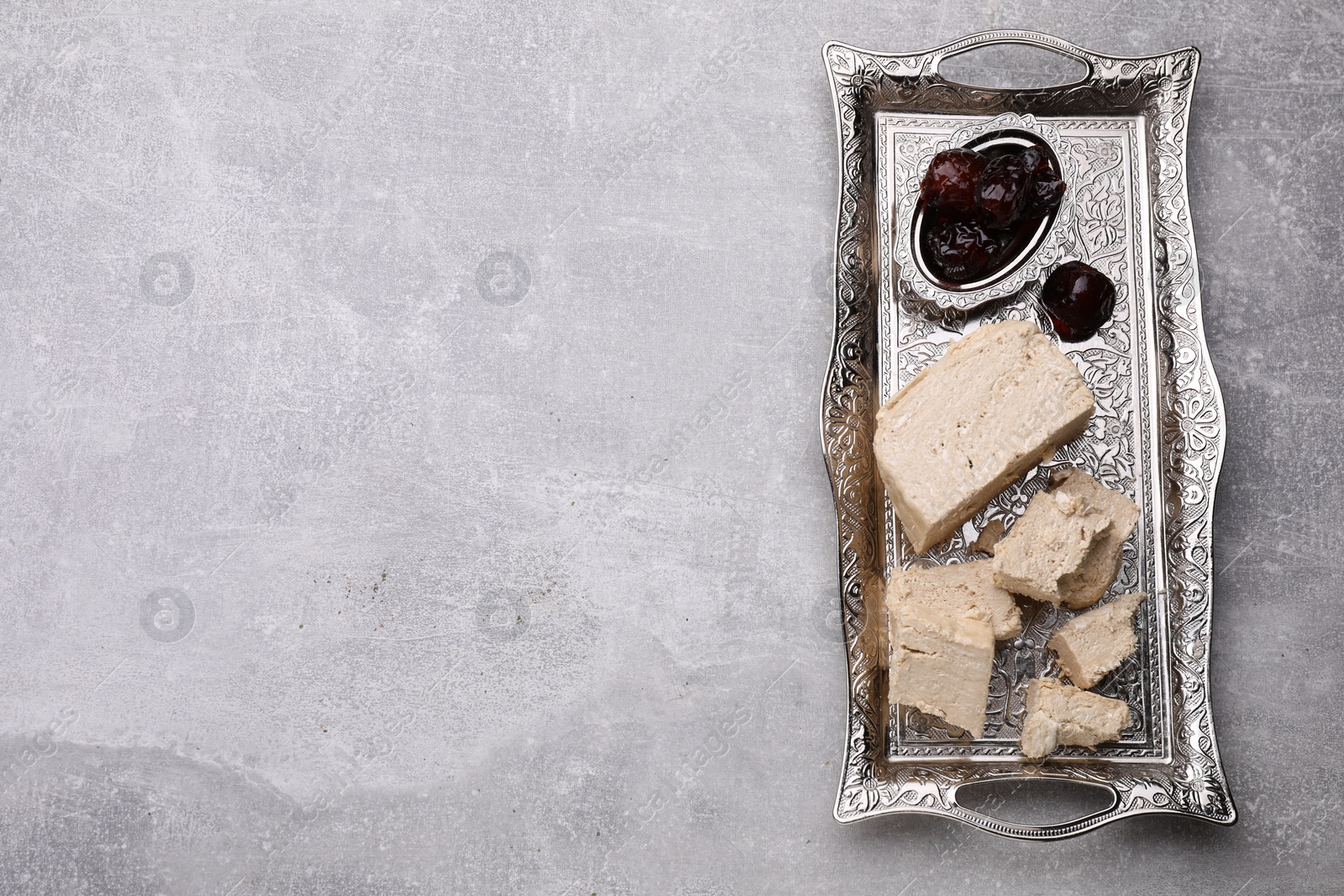 Photo of Pieces of tasty halva and dates served in vintage tea set on light grey table, top view. Space for text