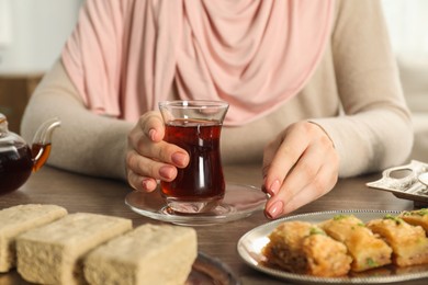 Photo of Woman with cup of delicious Turkish tea at wooden table, closeup