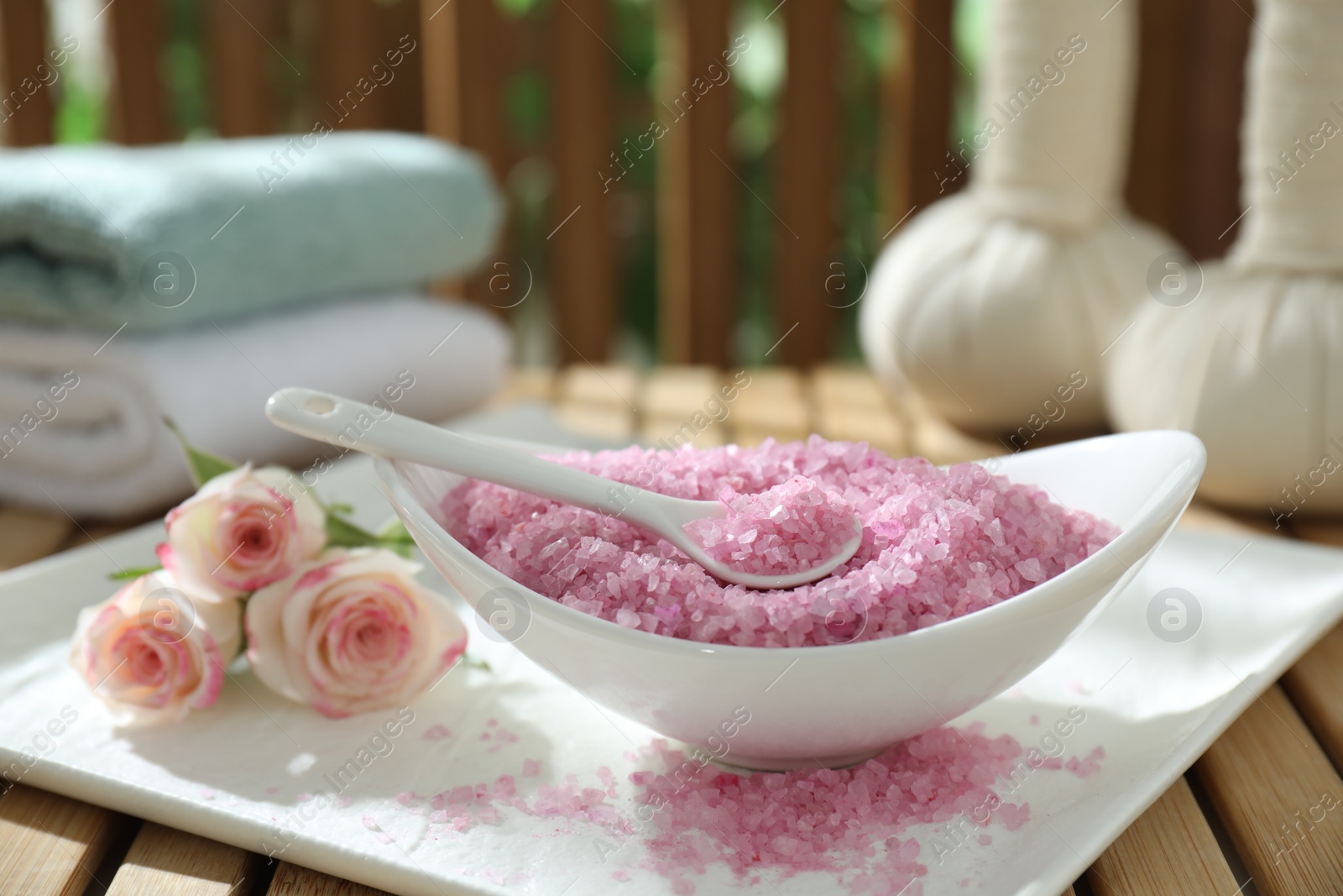 Photo of Bowl of pink sea salt and beautiful roses on wooden table, closeup