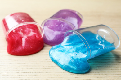 Photo of Overturned plastic containers with bright slimes on wooden background, closeup