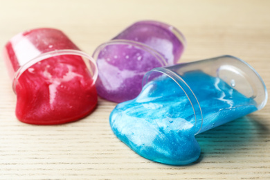 Overturned plastic containers with bright slimes on wooden background, closeup