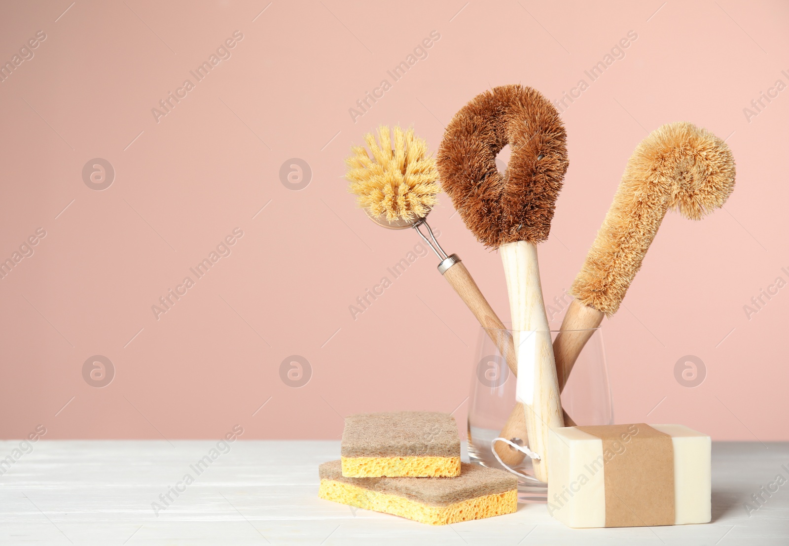 Photo of Cleaning brushes, soap bar and sponges on white wooden table against pink background, space for text. Dish washing supplies