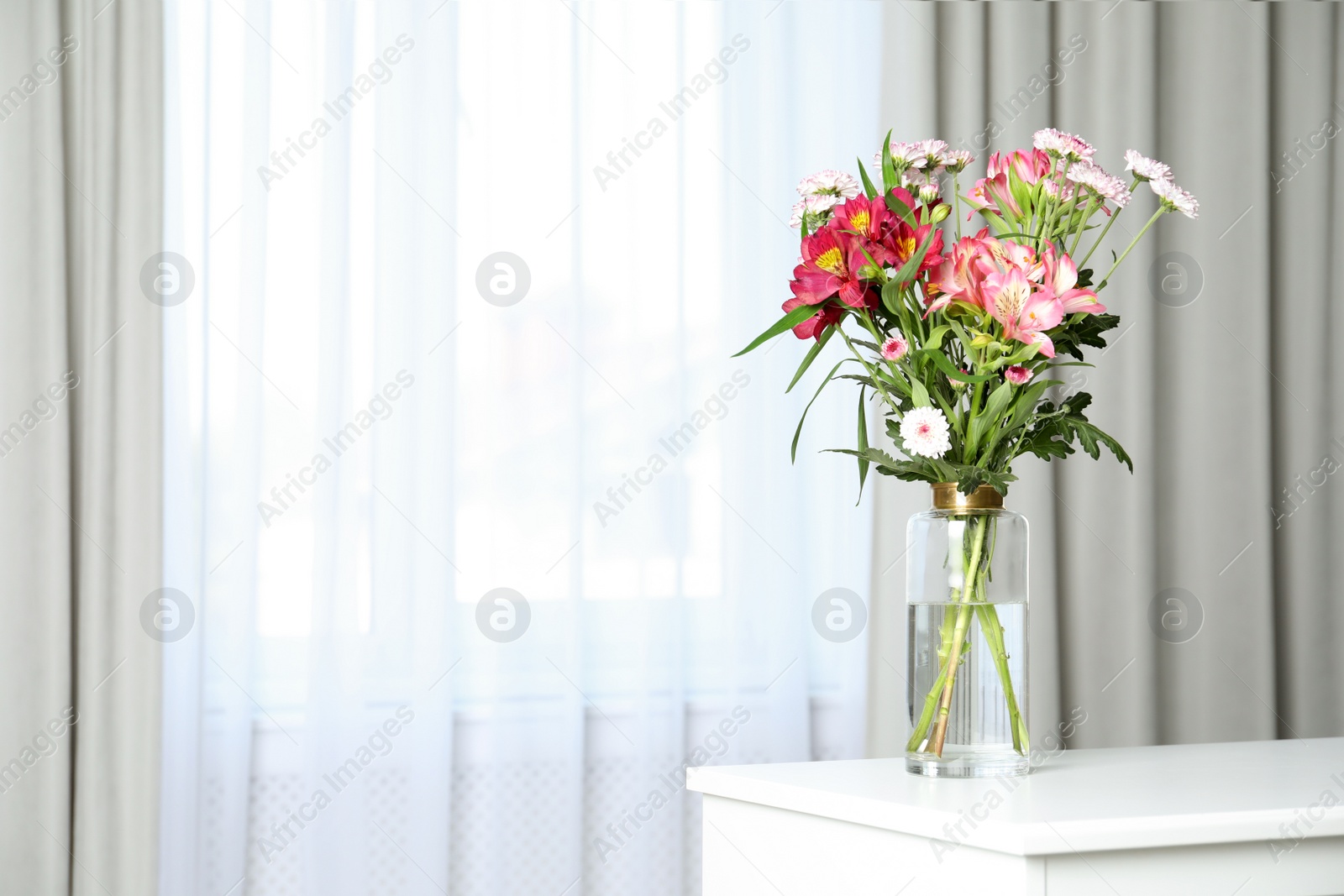 Photo of Vase with beautiful flowers on table near window indoors, space for text. Stylish element of interior design