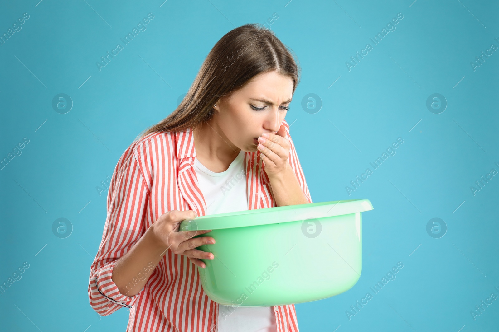 Photo of Woman with basin suffering from nausea on light blue background. Food poisoning