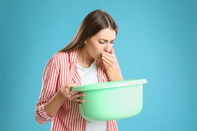 Woman with basin suffering from nausea on light blue background. Food poisoning