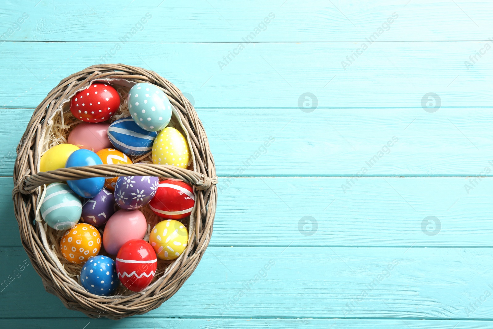 Photo of Wicker basket with painted Easter eggs on wooden background, top view. Space for text