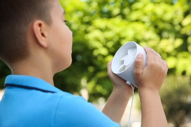 Photo of Little boy with portable fan outdoors, closeup. Summer heat