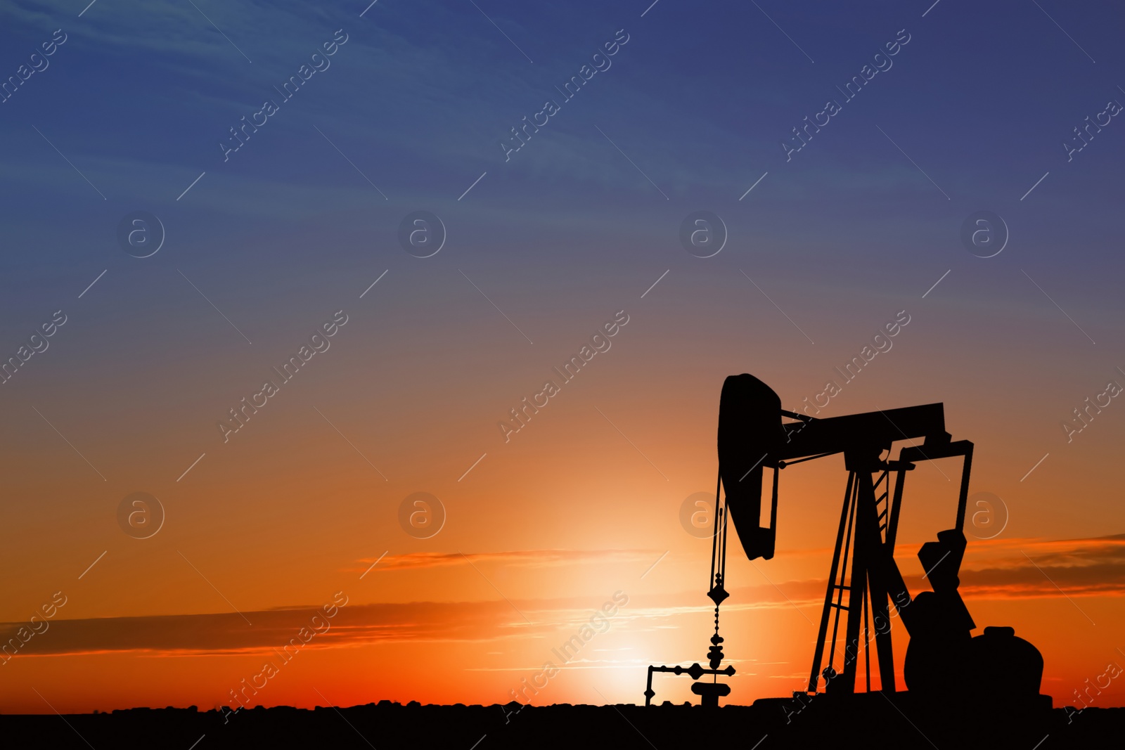Image of Silhouette of crude oil pump at sunset. Space for text