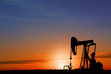 Image of Silhouette of crude oil pump at sunset. Space for text