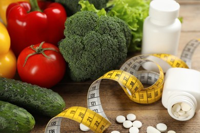 Weight loss pills, different vegetables and measuring tape on wooden table