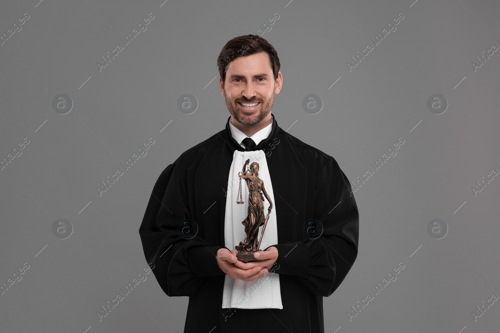 Photo of Smiling judge with figure of Lady Justice on grey background