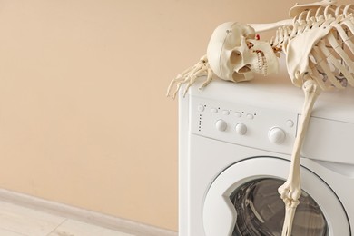 Photo of Waiting concept. Human skeleton lying on washing machine near beige wall indoors, space for text