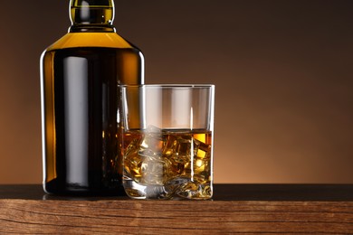 Photo of Whiskey with ice cubes in glass and bottle on wooden table, closeup. Space for text