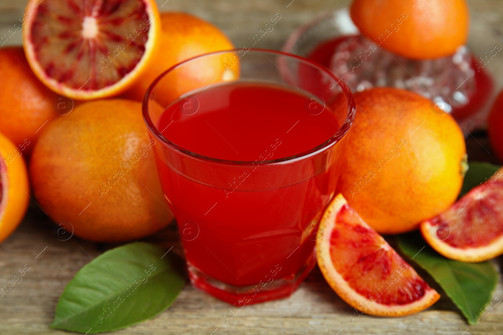 Photo of Tasty sicilian orange juice in glass and fruits on wooden table