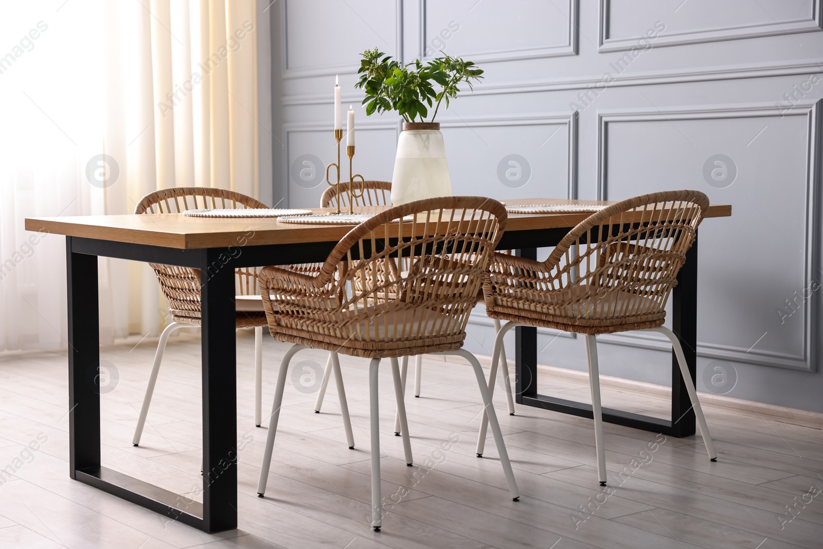 Photo of Rattan chairs, table, burning candles and vase with green branches in stylish dining room