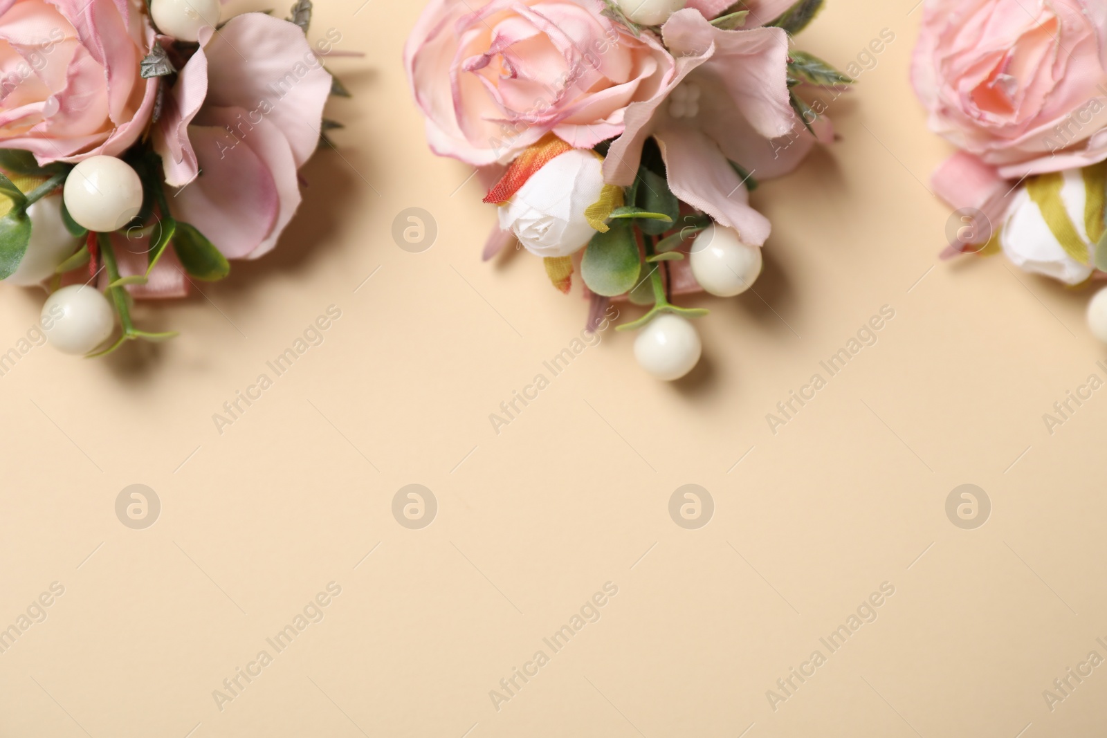 Photo of Stylish pink boutonnieres on beige background, flat lay. Space for text