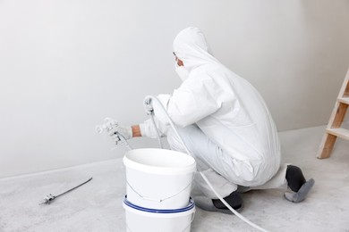 Photo of Decorator painting white wall with spray indoors