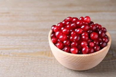 Photo of Fresh ripe cranberries in bowl on wooden table. Space for text