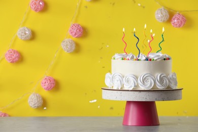 Photo of Birthday cake with burning candles on table near yellow wall, space for text