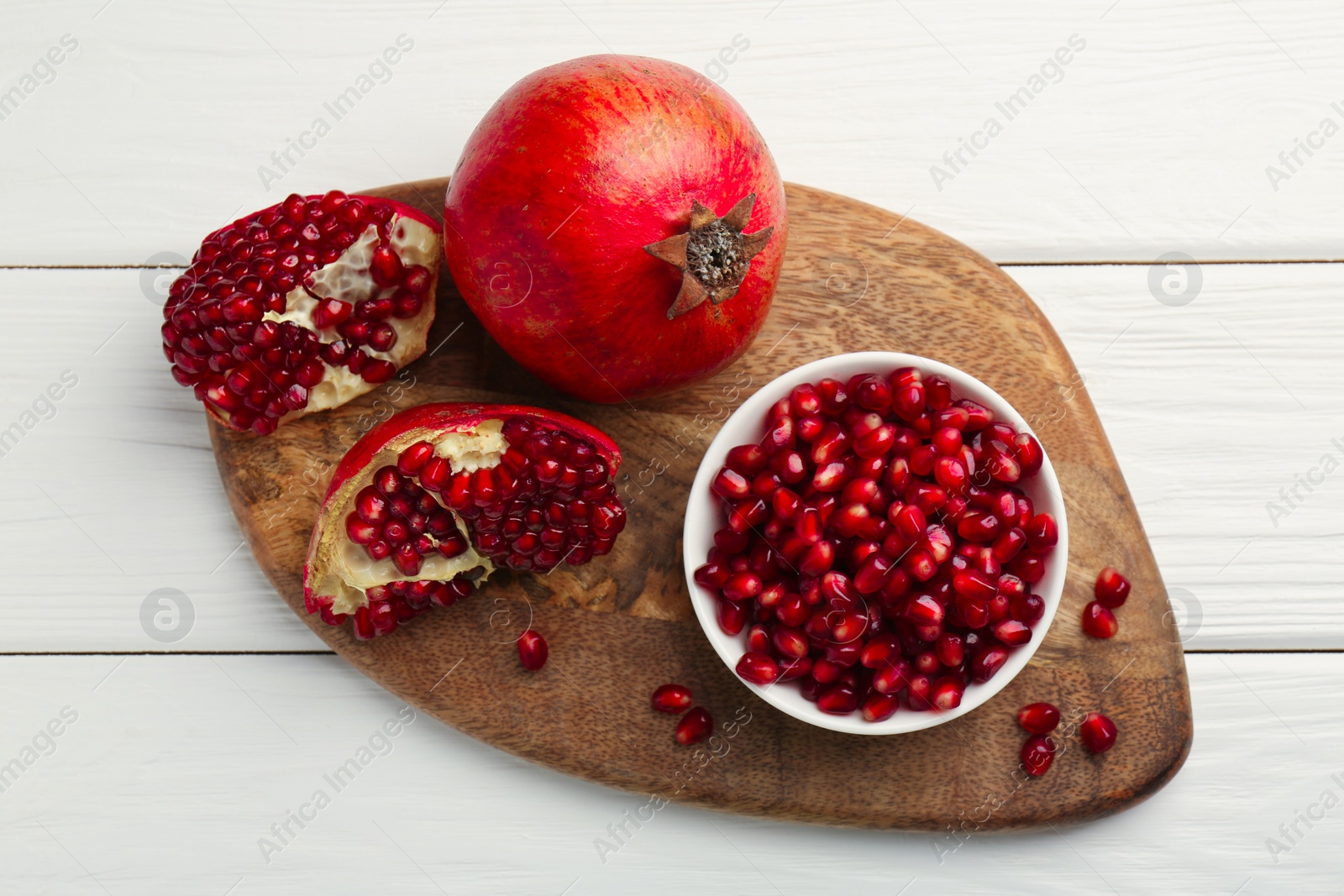 Photo of Ripe juicy pomegranate with grains on white wooden table, top view