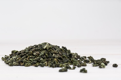 Photo of Heap of dried green tea leaves on white table