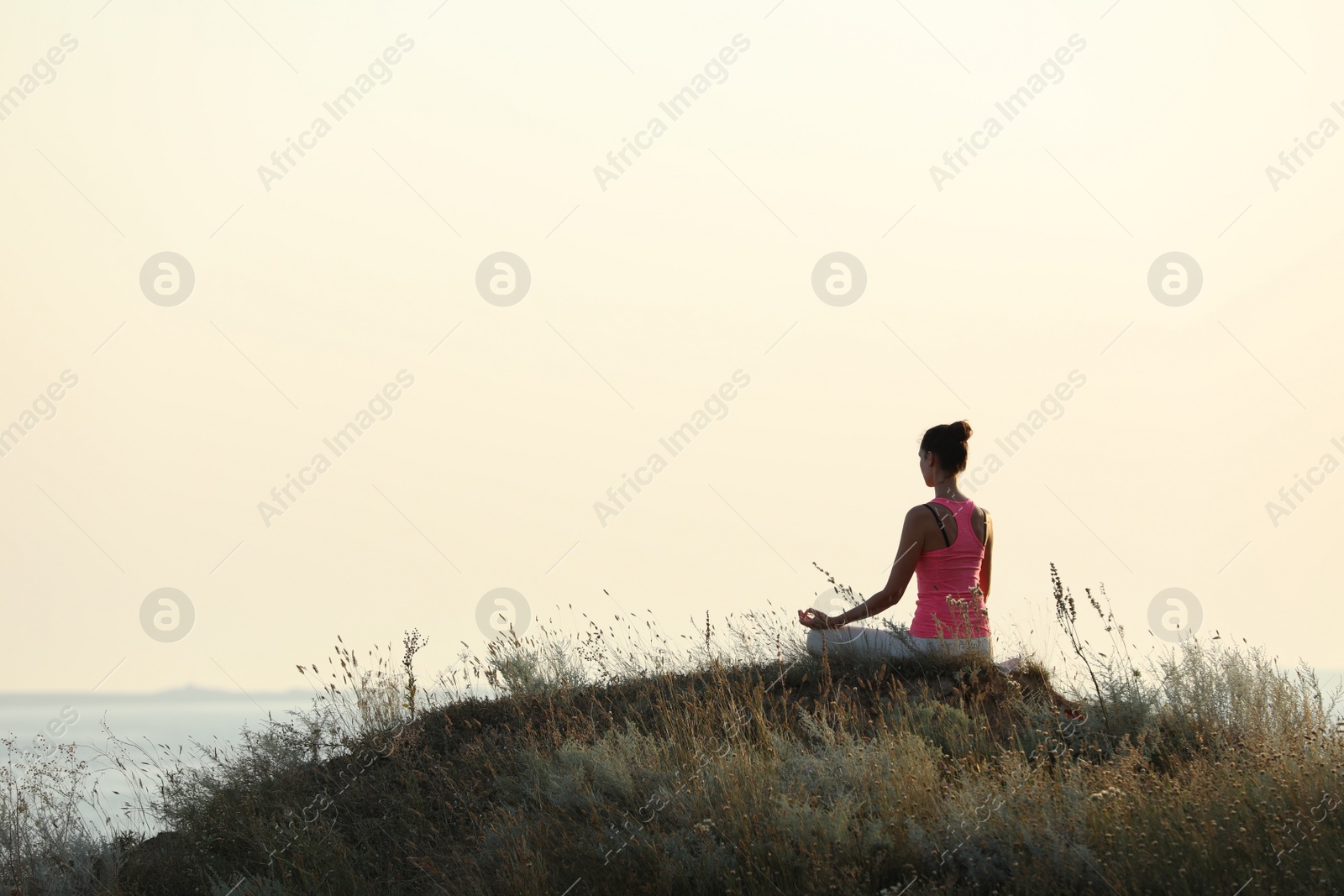 Photo of Woman meditating on hill near sea, back view. Space for text